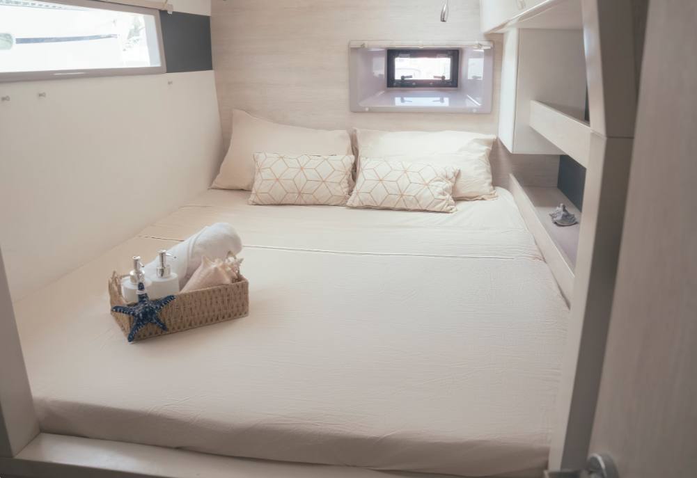 A double guest cabin with patterned pillows, folded towels and an overhead skylight hatch