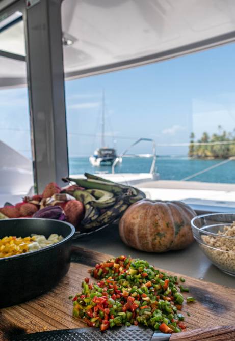 Colorful diced peppers, pumpkin and grains prepped on a cutting board with the sea framed by the saloon window